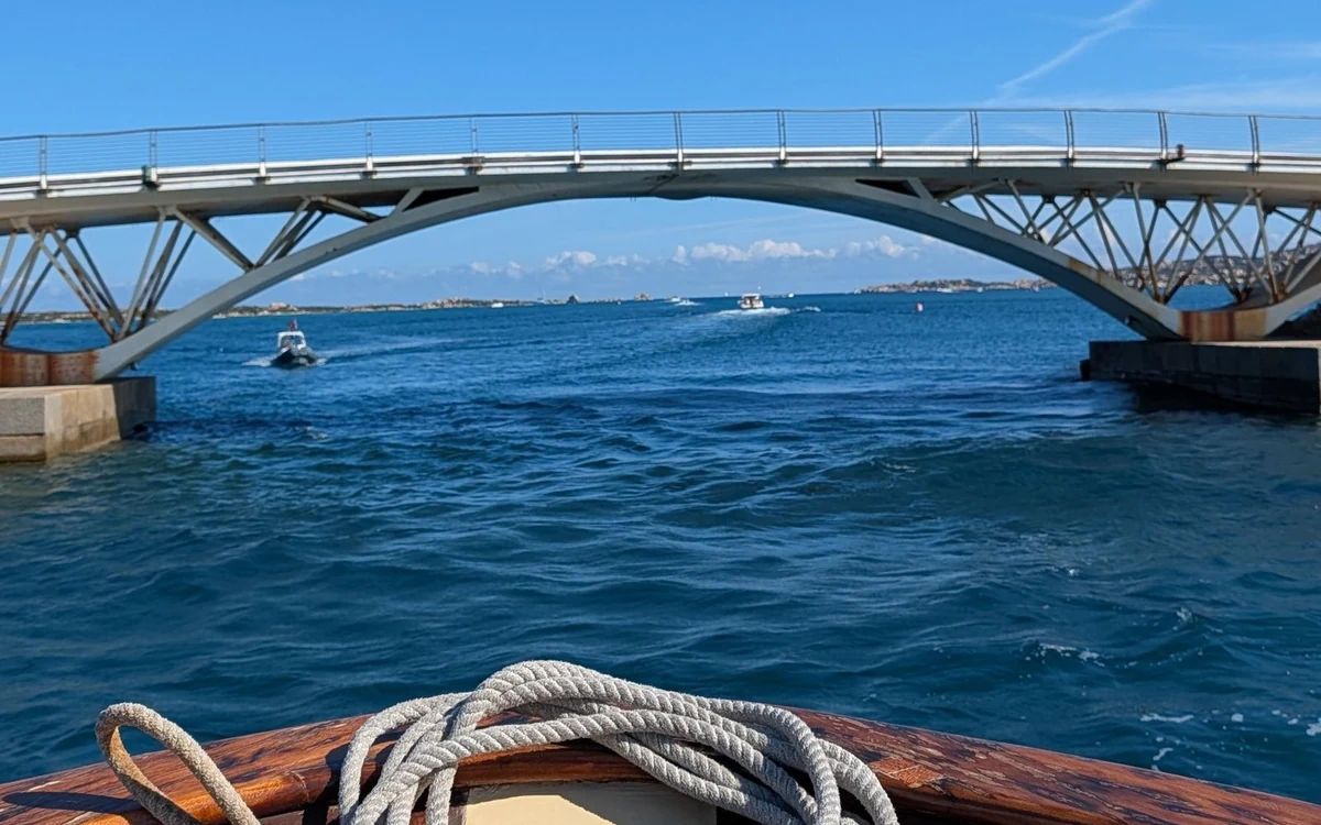 A wooden bow with a coil of rope heading toward a steel arch bridge over open blue water