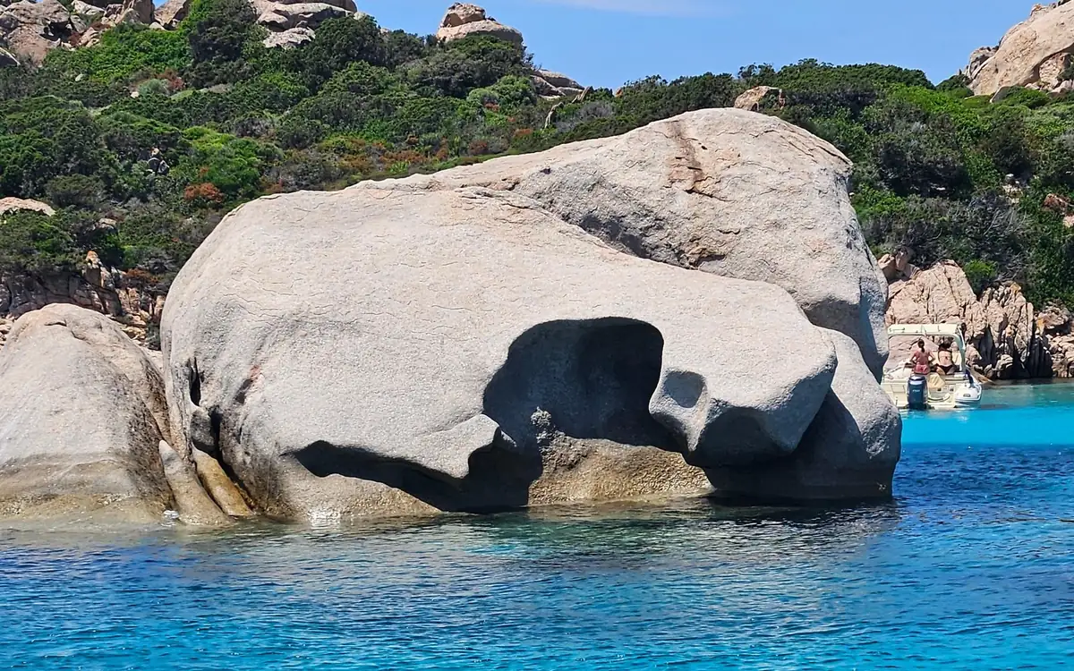A smooth grey granite boulder with a hollow, standing in clear blue water
