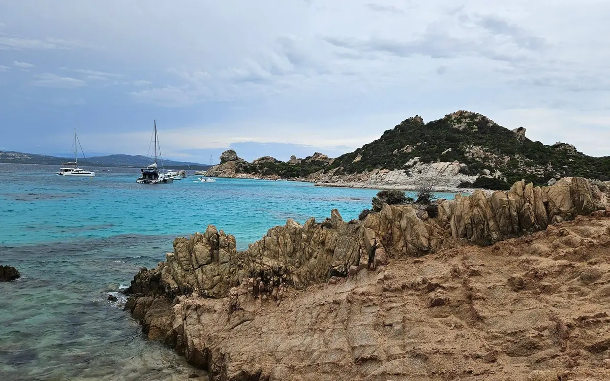Jagged granite rocks in the foreground and sailboats moored in a bay