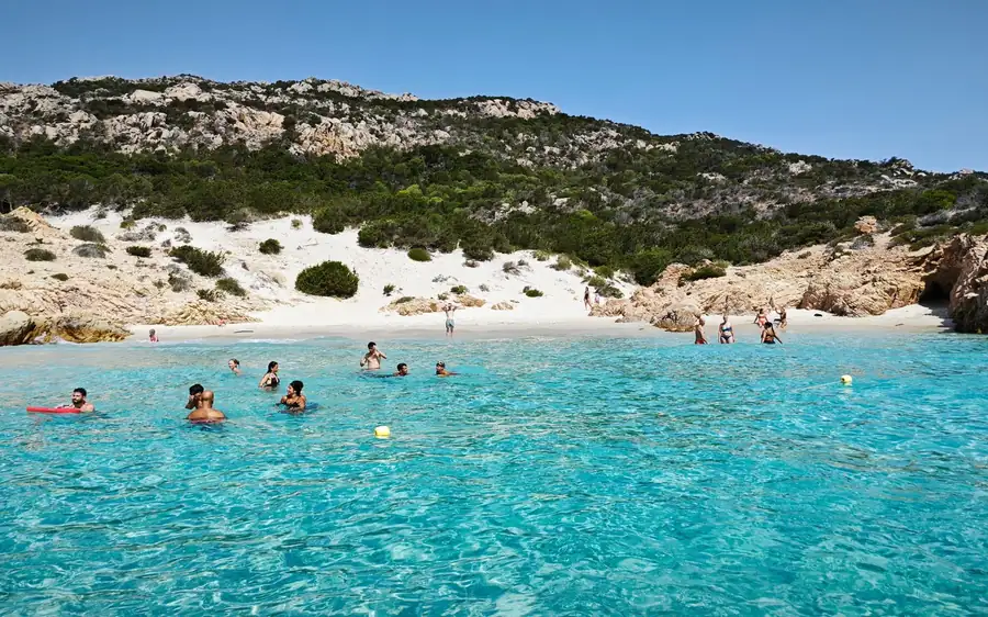 Swimmers in turquoise shallows off a white sand beach