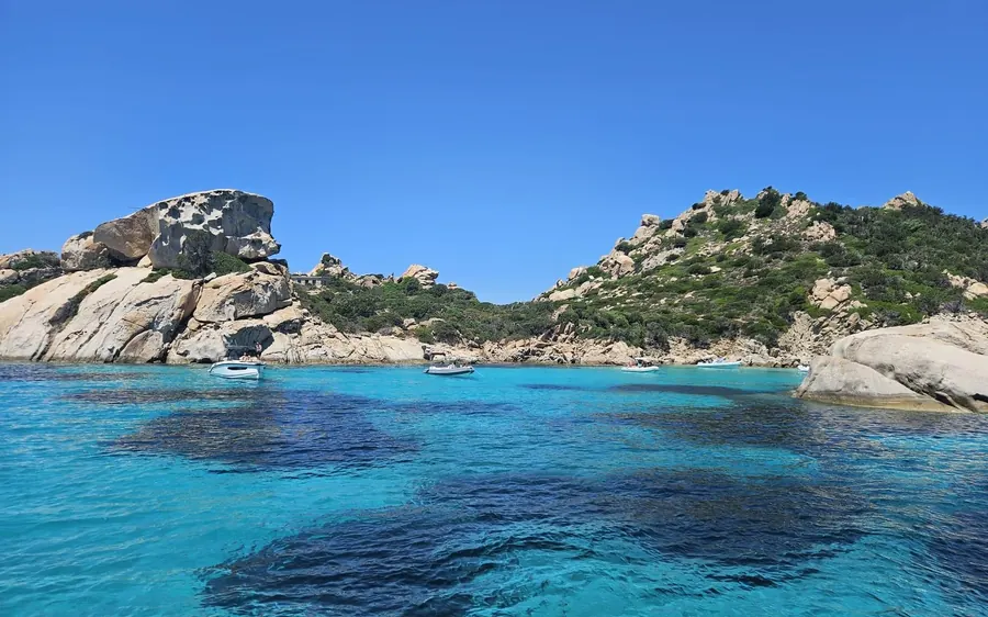 Small boats anchored in a turquoise bay below granite rocks
