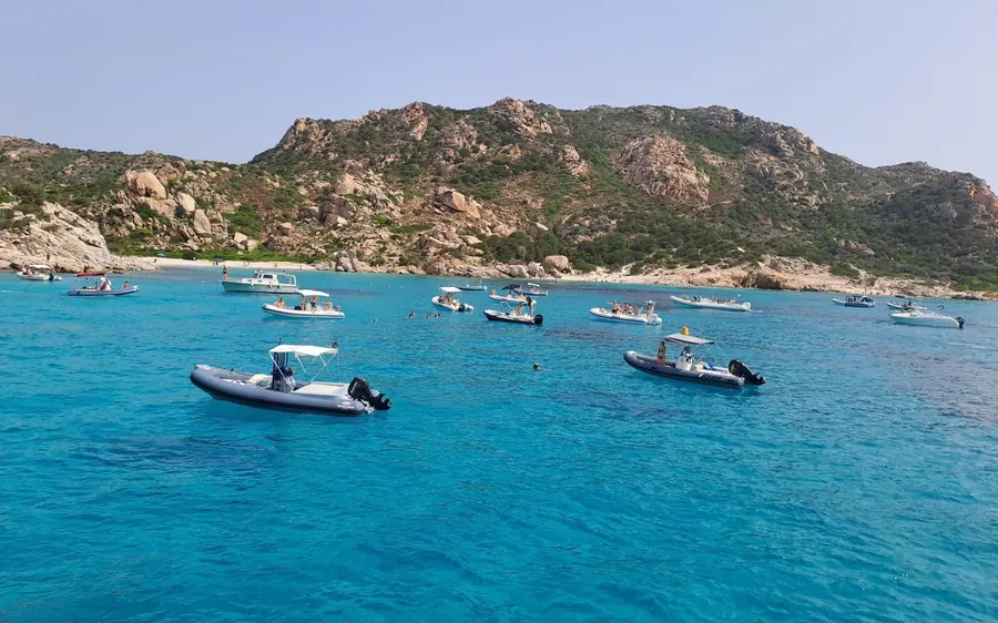 Inflatable boats anchored in turquoise water below a rocky island
