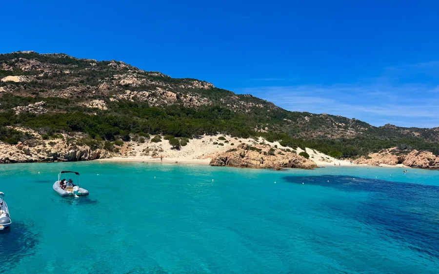 A sandy beach and turquoise bay below scrub-covered hills