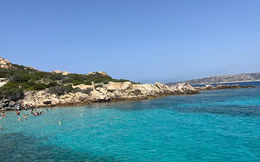 Swimmers in turquoise water off a low granite shore