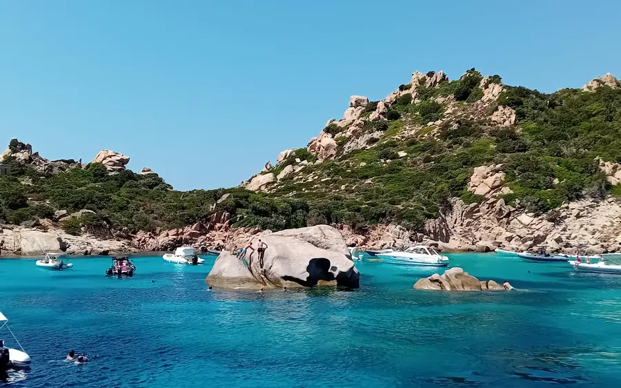 Boats anchored around a rounded granite boulder in a turquoise bay