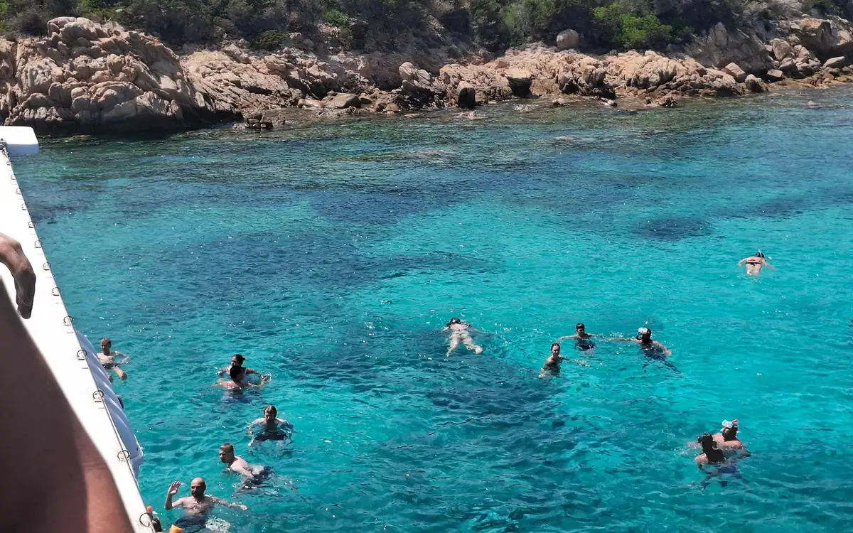 Swimmers in clear water beside the hull of a tour boat