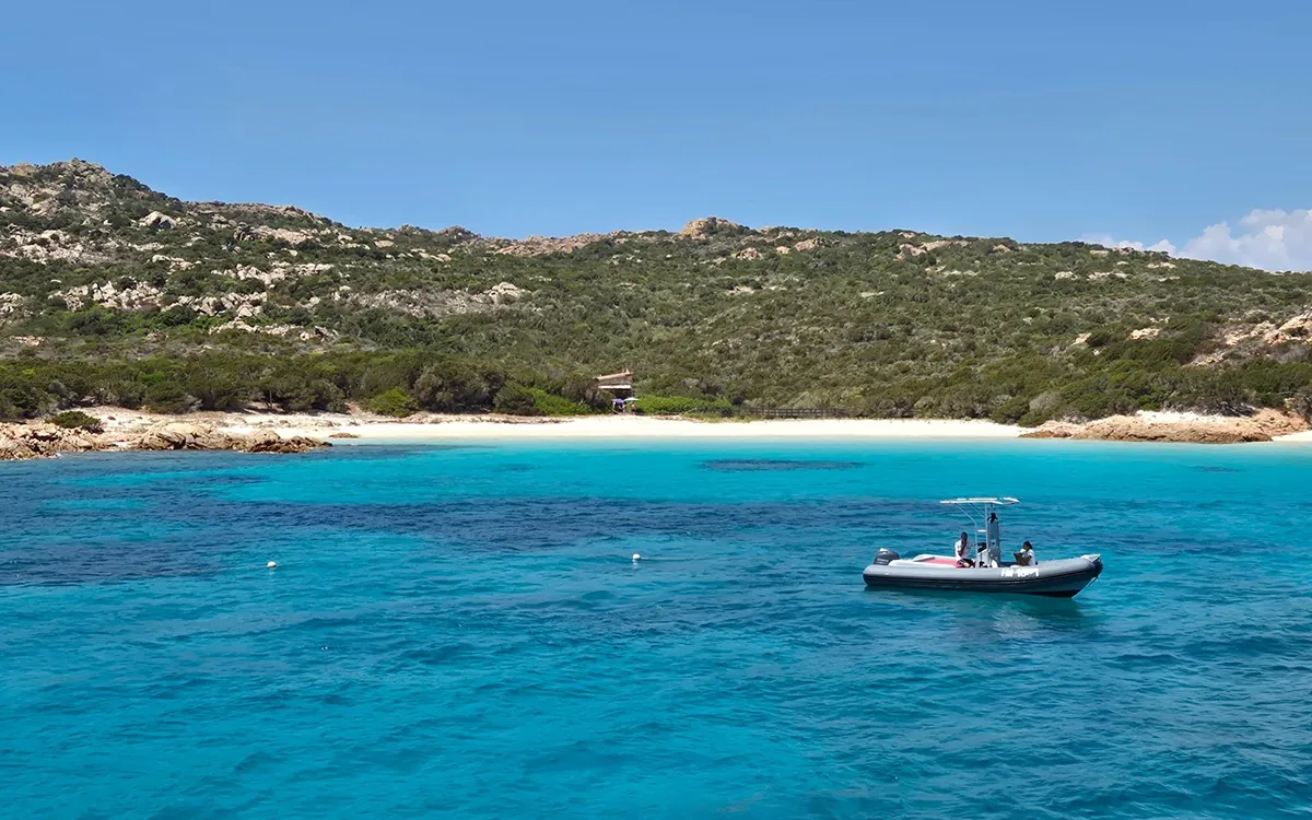 A small white motorboat in a turquoise bay below a white beach